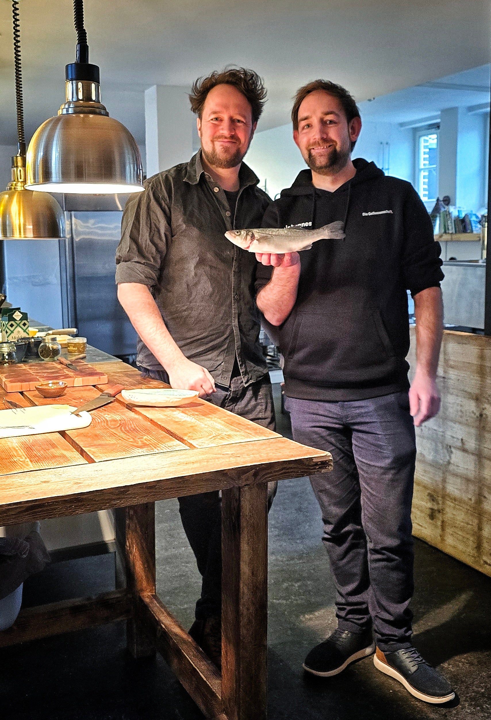 Elias Eckel und Johannes Wolf in der Kochschule E.ssenz mit einem Wolfsbarsch in der Hand