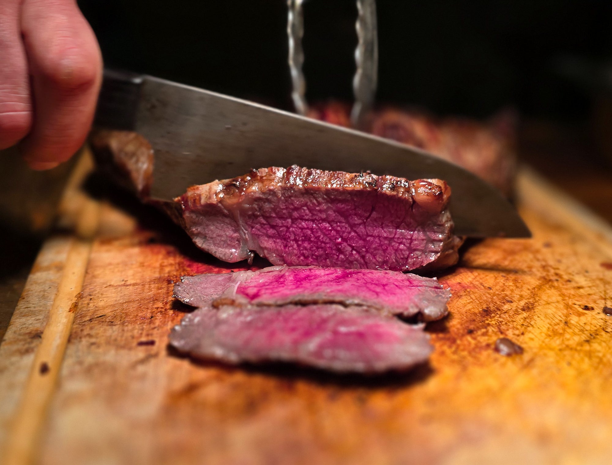 Steak in rosa, welches geschnitten wird von einem großen Messer und Hand. Es liegt auf einem Holzbrett