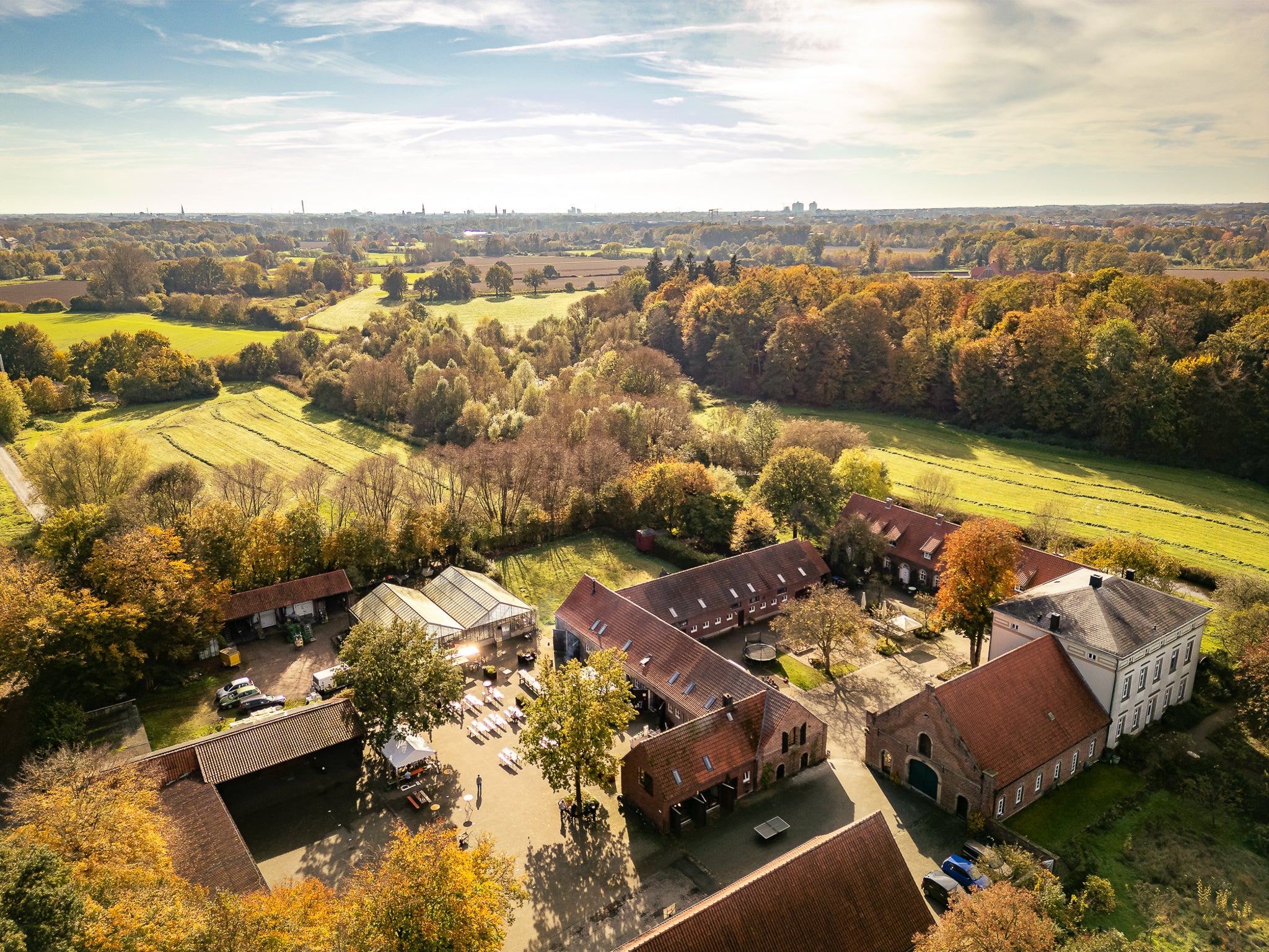 Eventlocation Münster, Luftaufnahme des ganzen Geländes von Hauscoerde und einer Outdoor-Veranstaltung bei Eckels Kladde. Drumherum sieht man wie ländlich gelegen das ist. Umringt ist das Gelände von grünen Feldern und vielen Bäumen.